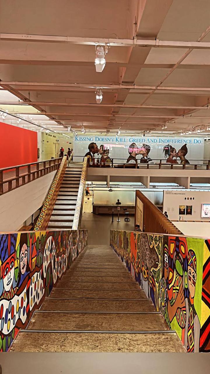 Interior de museu com arte urbana colorida nas laterais, escadas e pessoas visitando